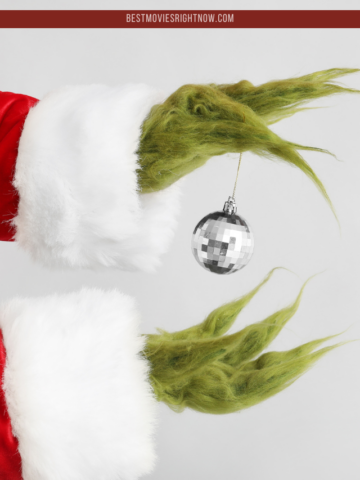 Green Hairy Hands of Creature in Santa Costume Holding Christmas Ball